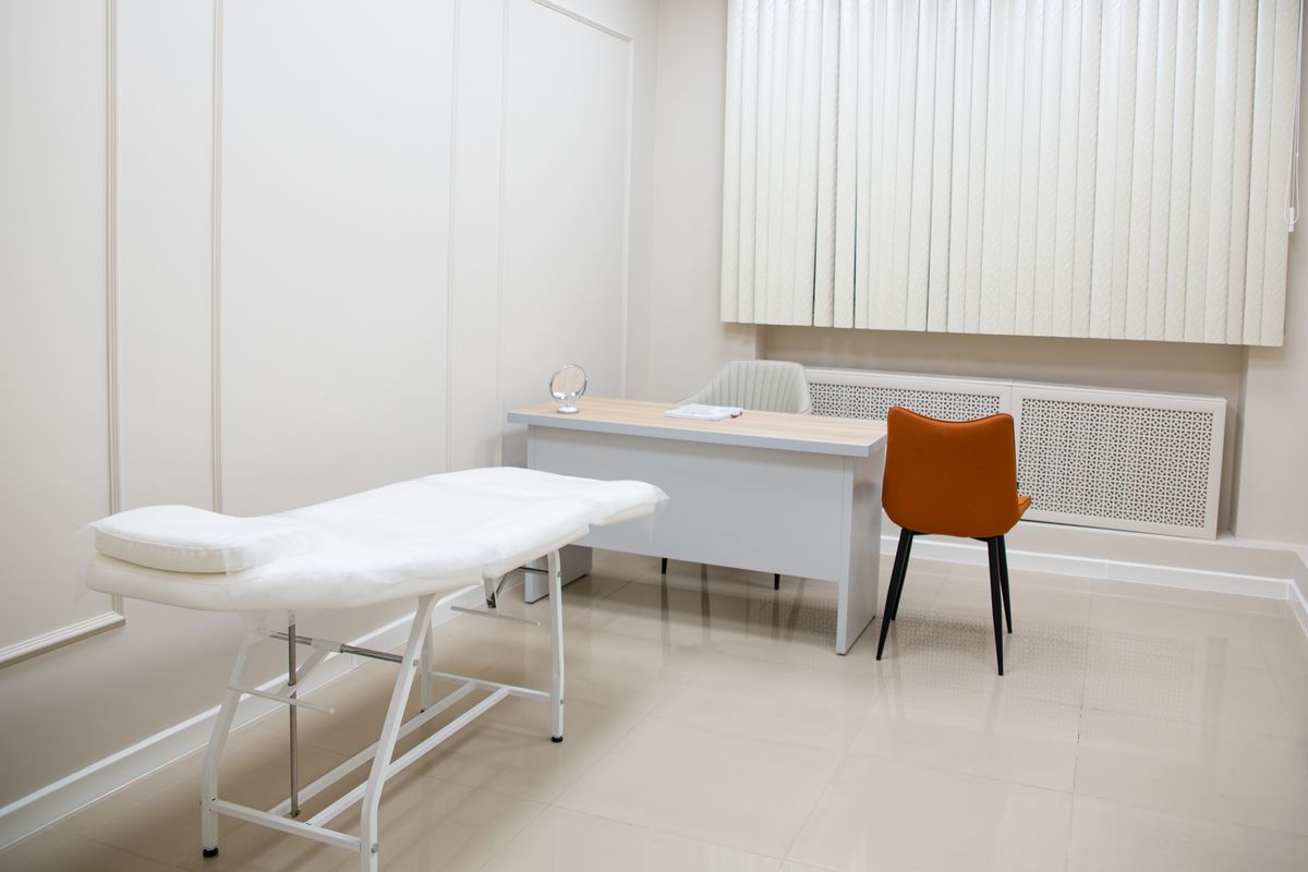 Minimalist medical examination room with desk, chairs, and an exam bed